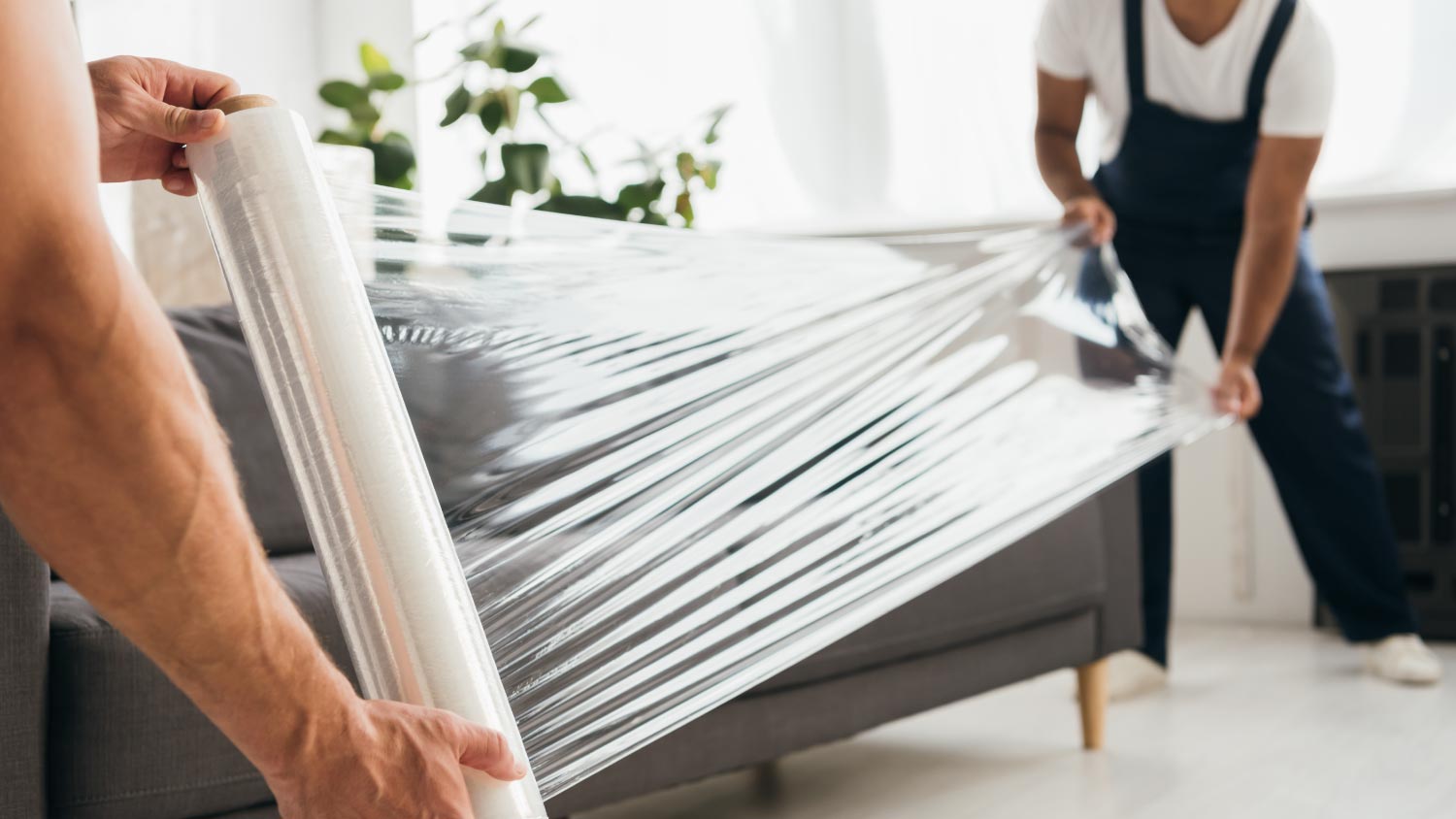 Movers holding stretch film roll near sofa