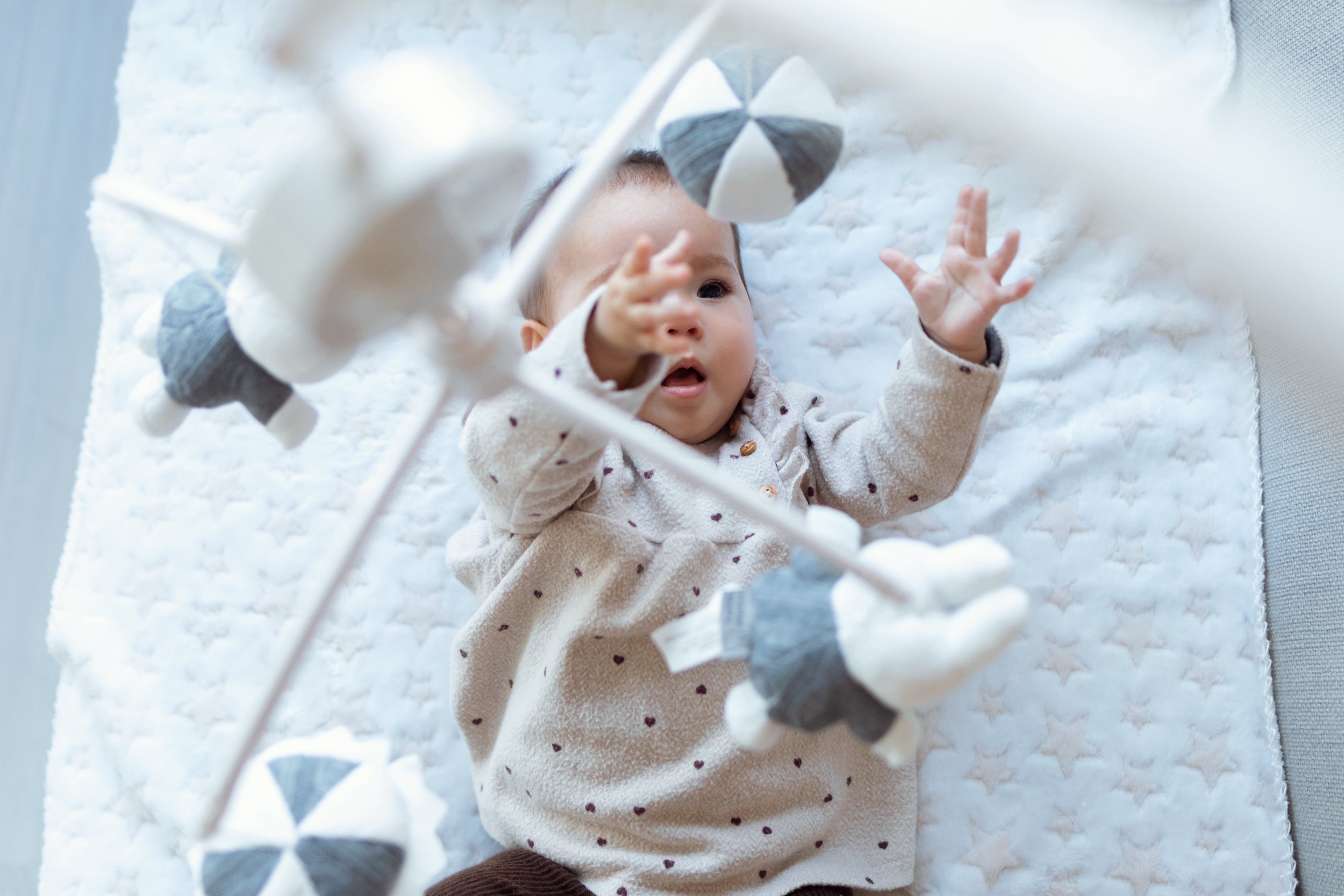 Baby in crib staring at hanging mobile