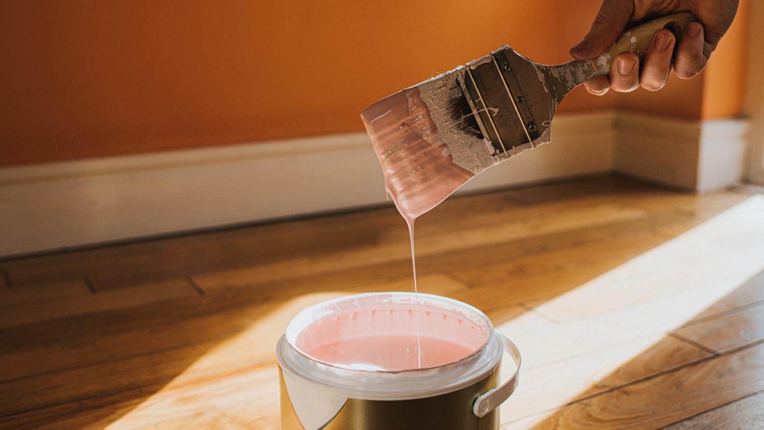 A paint brush into a large tin of pink paint