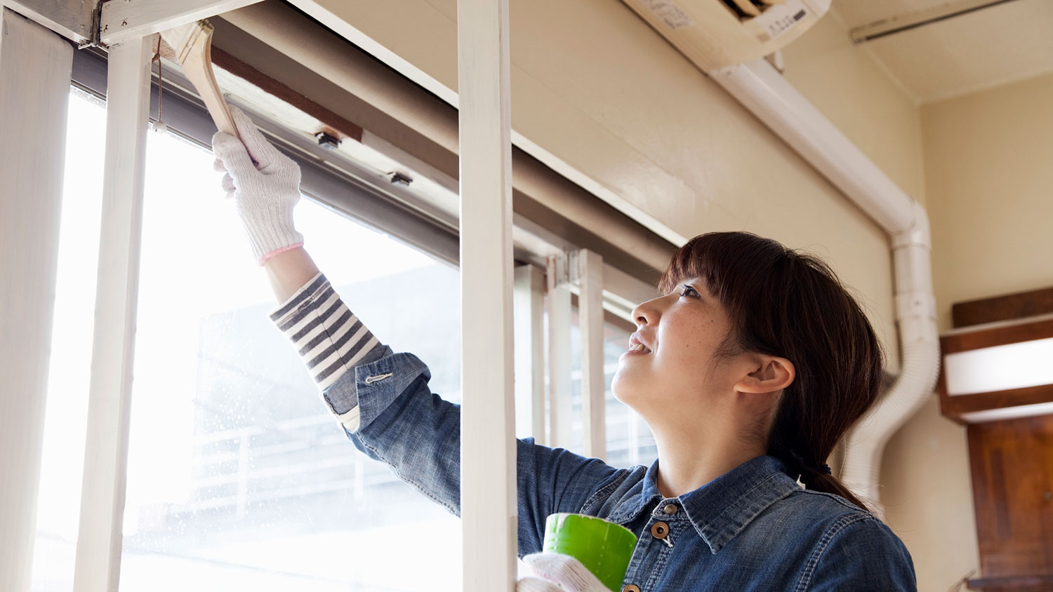 Woman painting wooden window frame with a brush