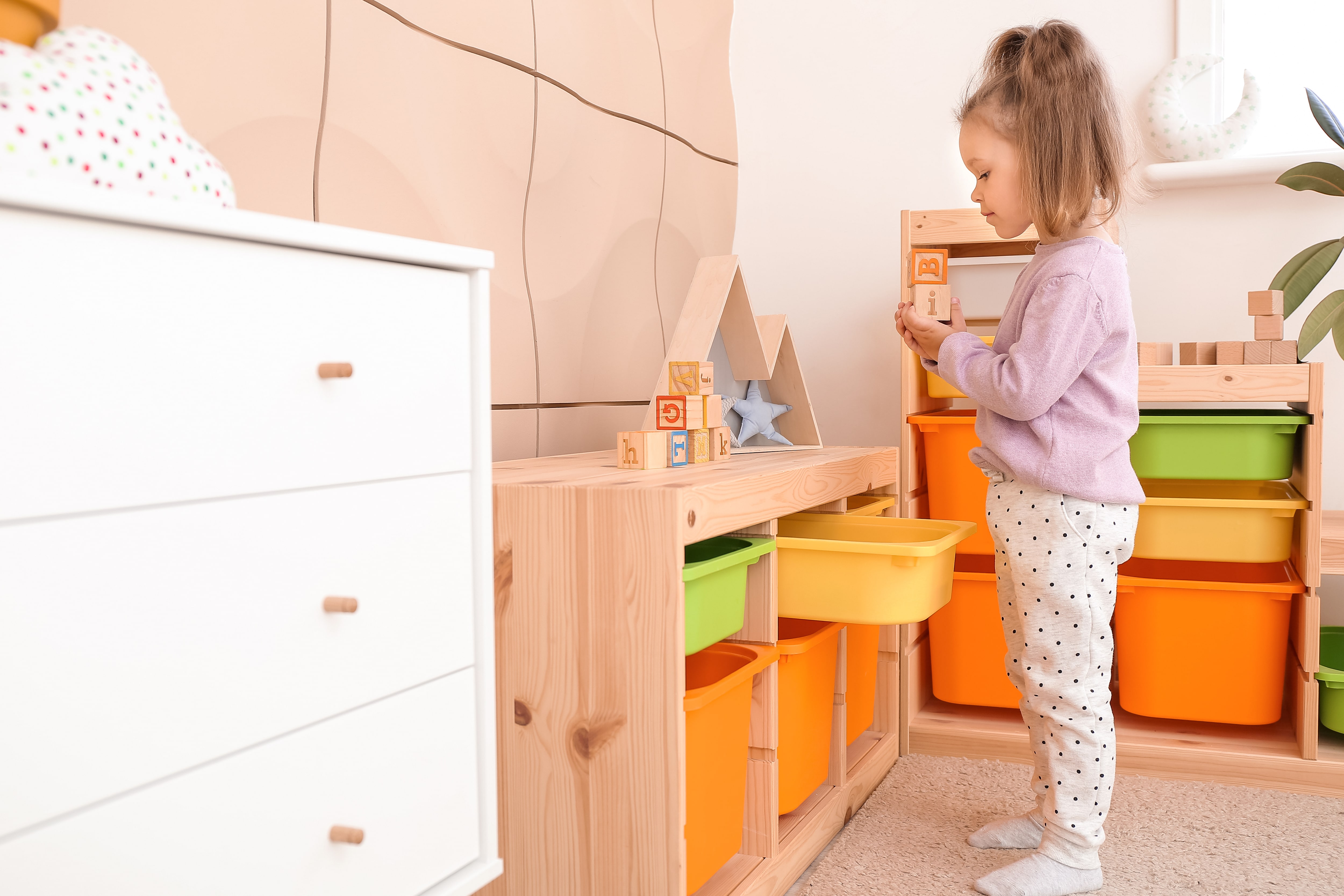 A young girl putting blocks away in a toy bin in a playroom