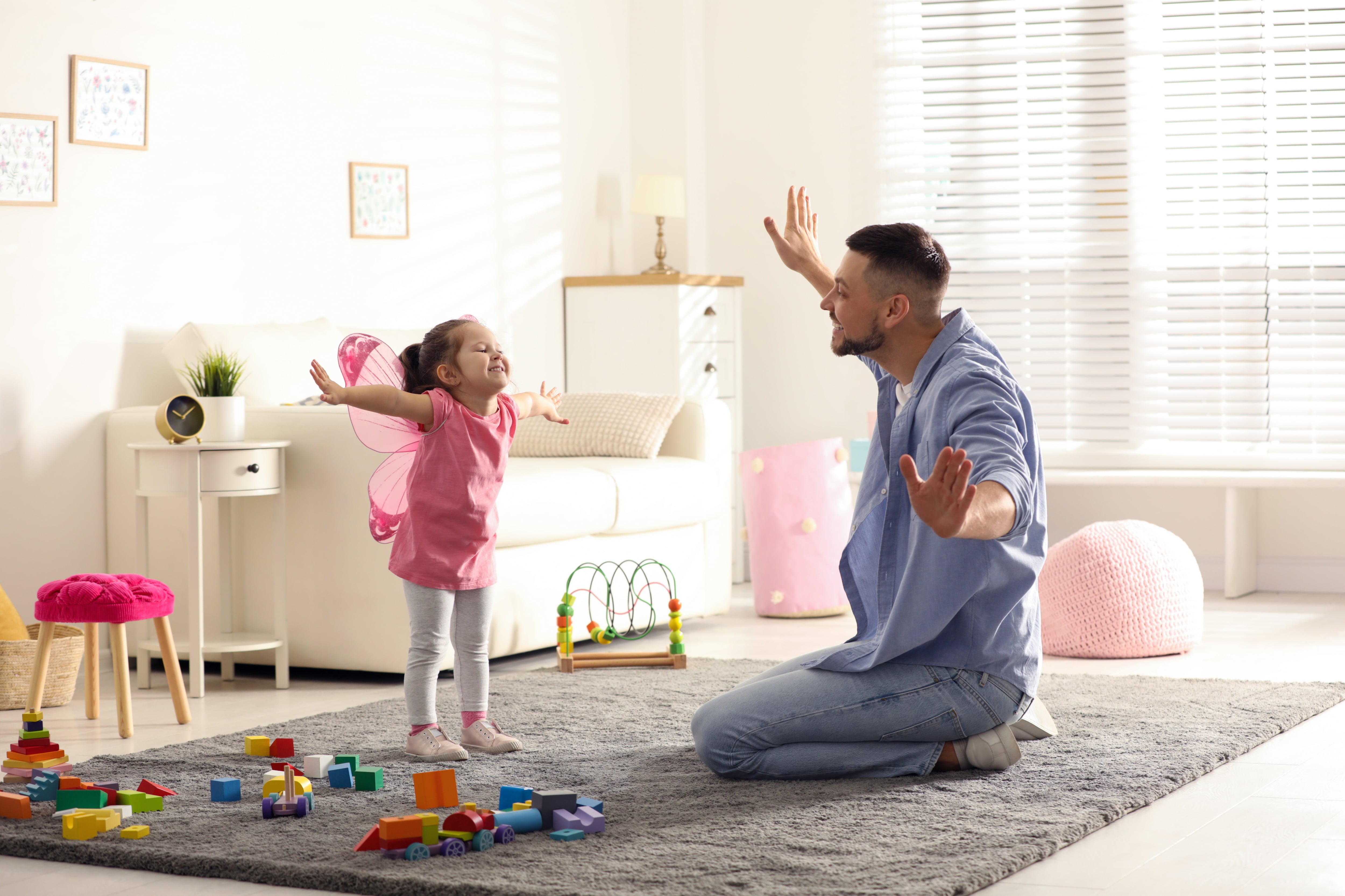 A father playing with his daughter in a room with a plush gray rug