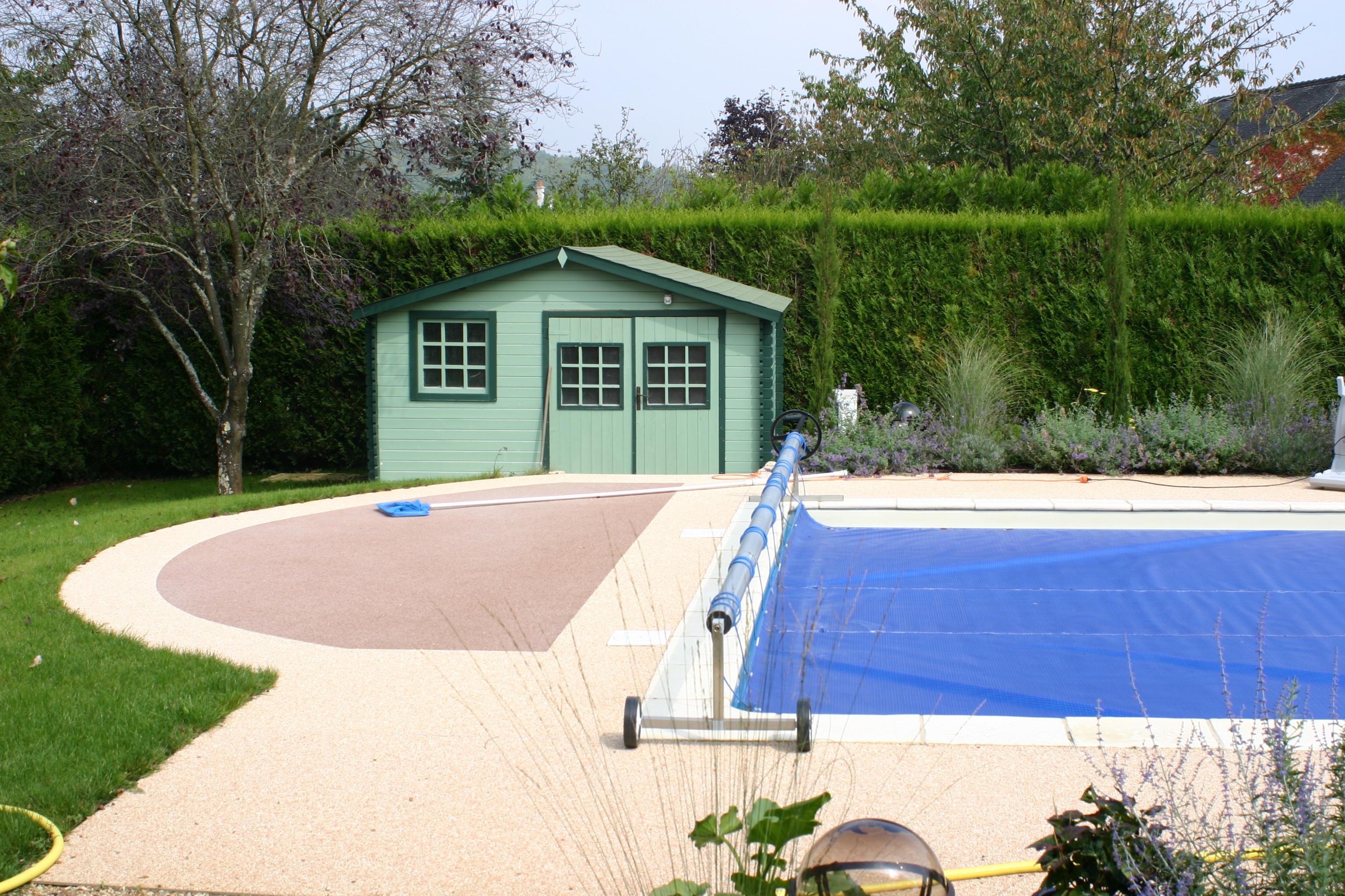 An inground pool with a green shed pool house