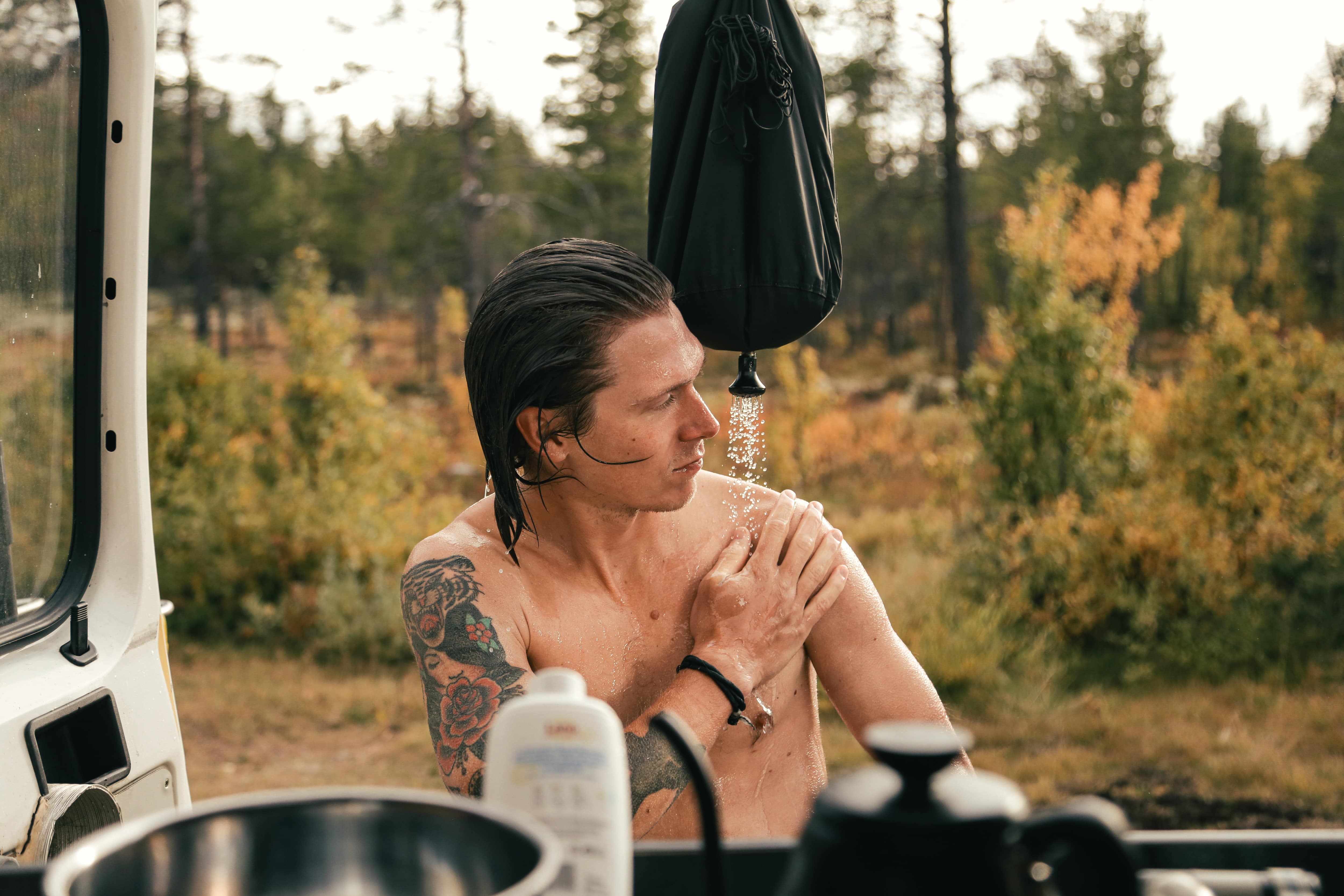 A man taking an outdoor shower from the back of a vehicle with a camp shower bag