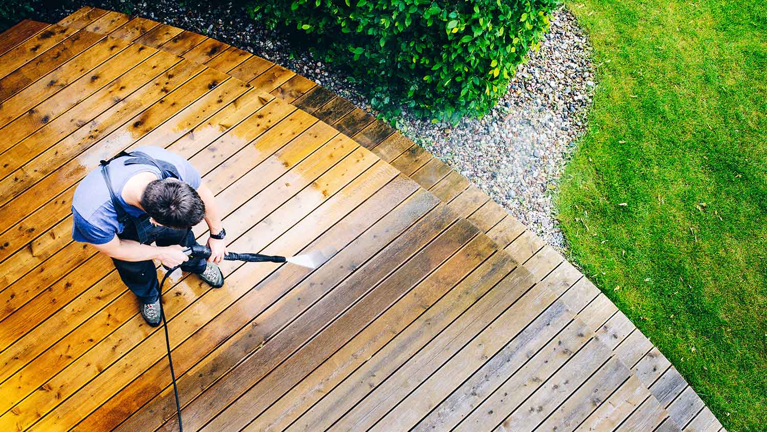 Man washing wood deck with power washer