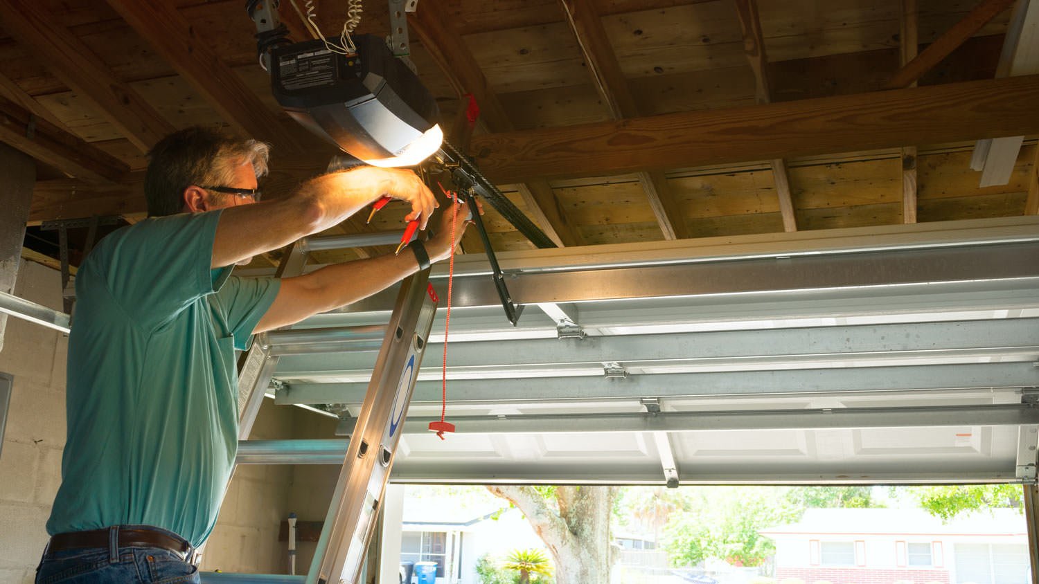 A professional on a ladder inspecting an open garage door