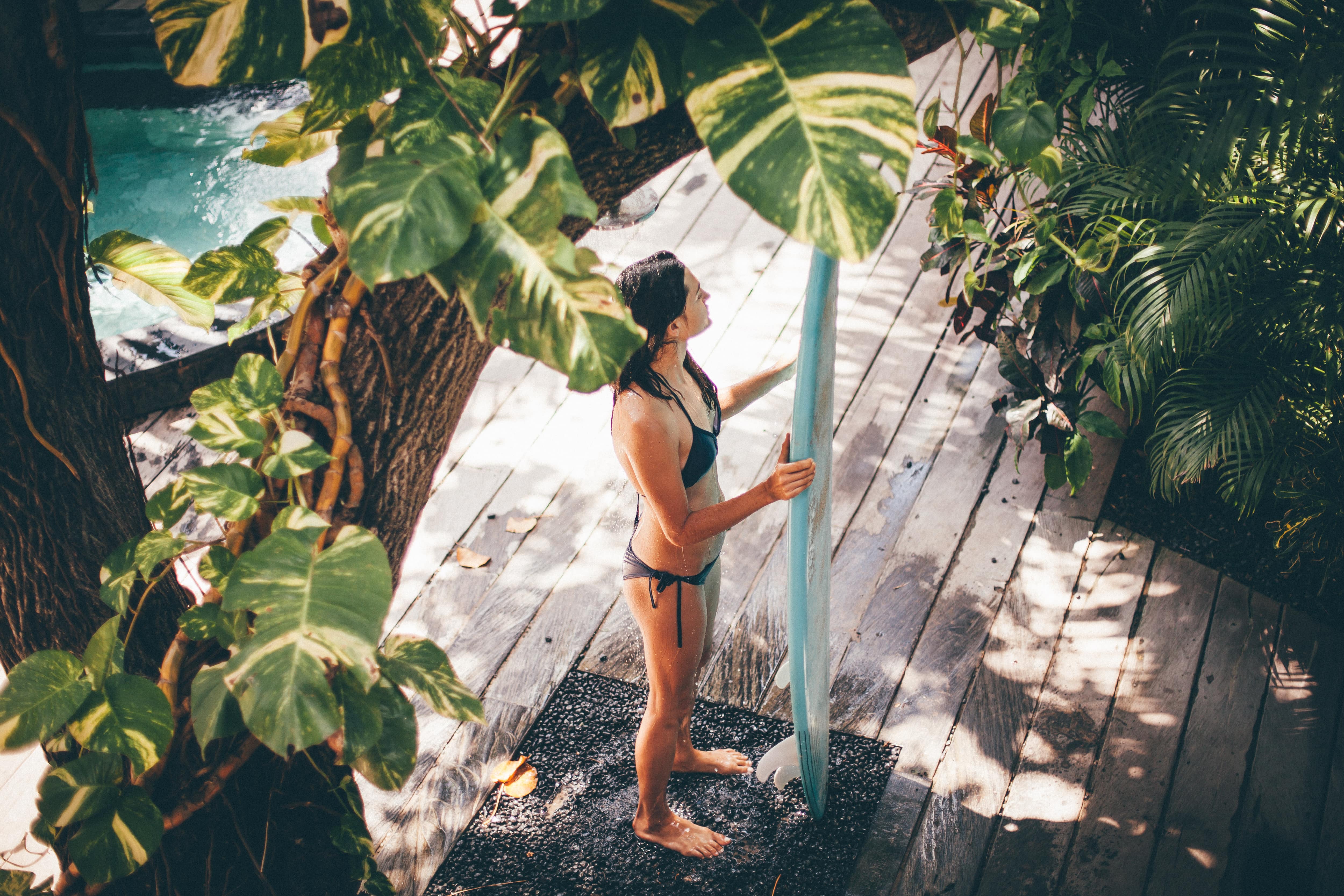 A woman rinsing off a surfboard in an outdoor shower