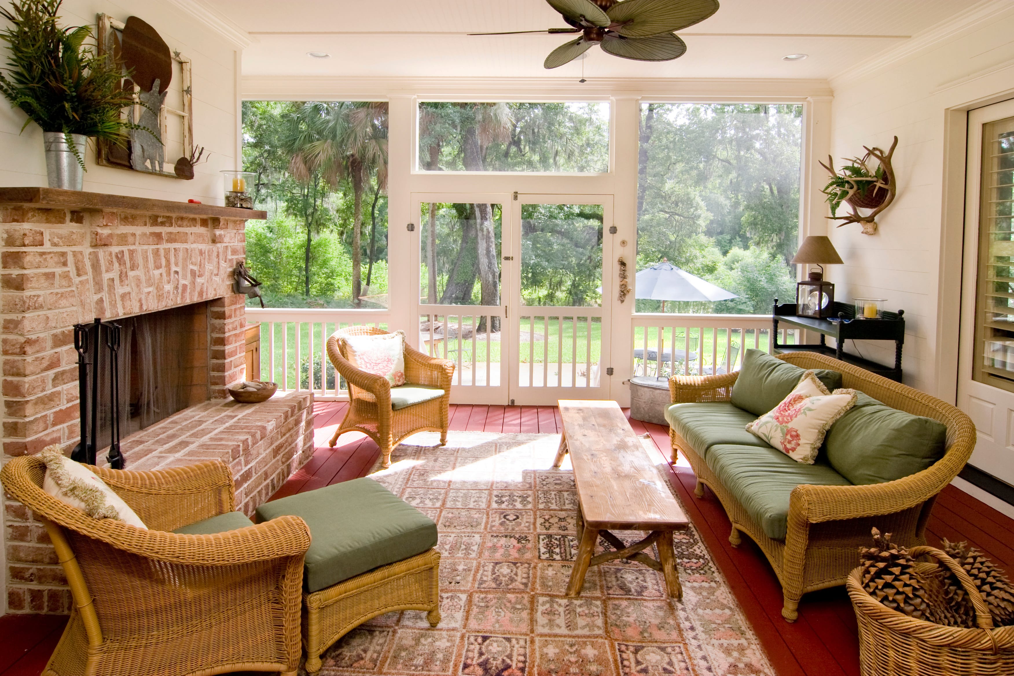 A screened-in living area with wicker furniture and a large brick fireplace