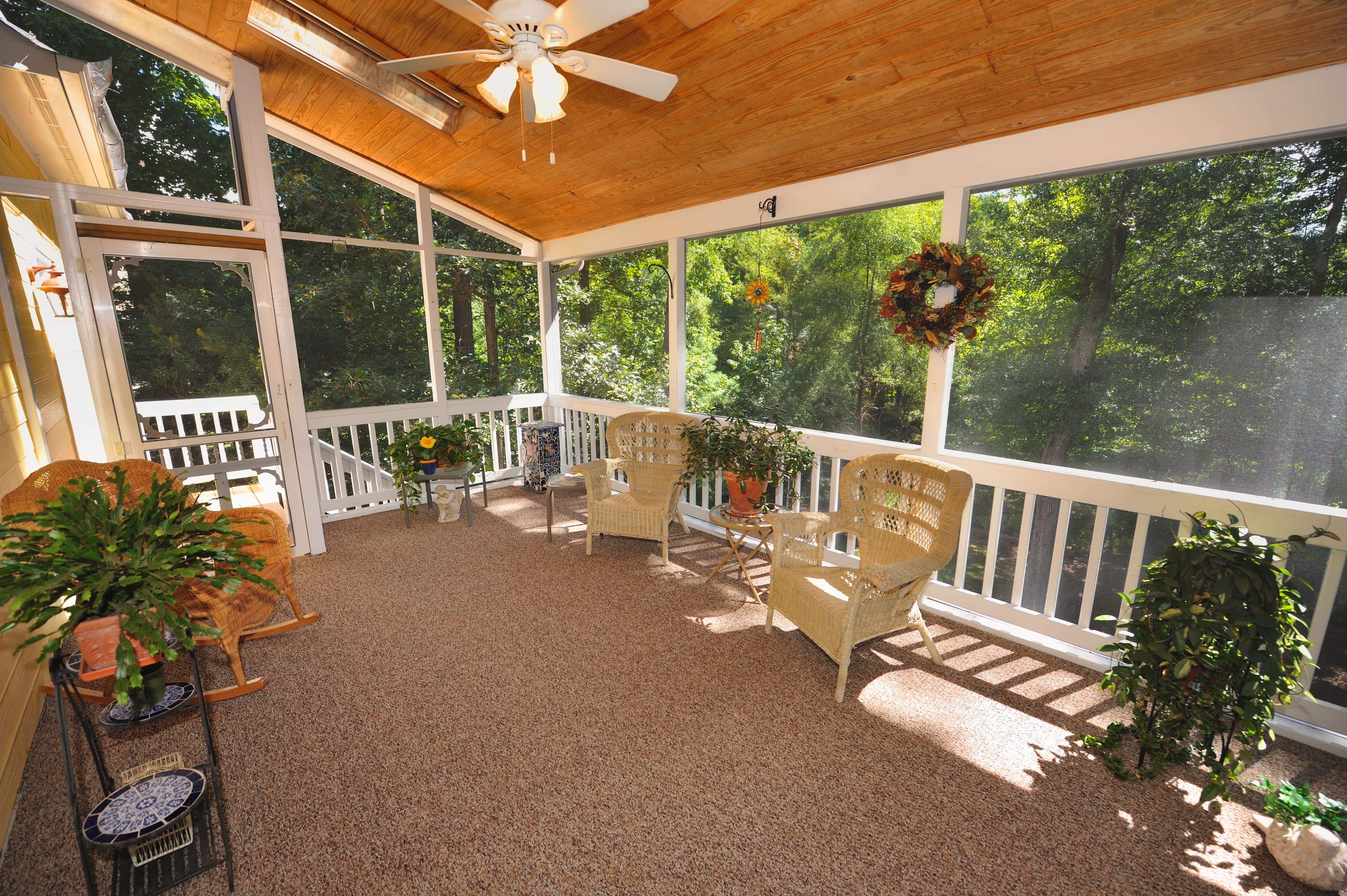 A large screened-in porch with wicker seating and several plants