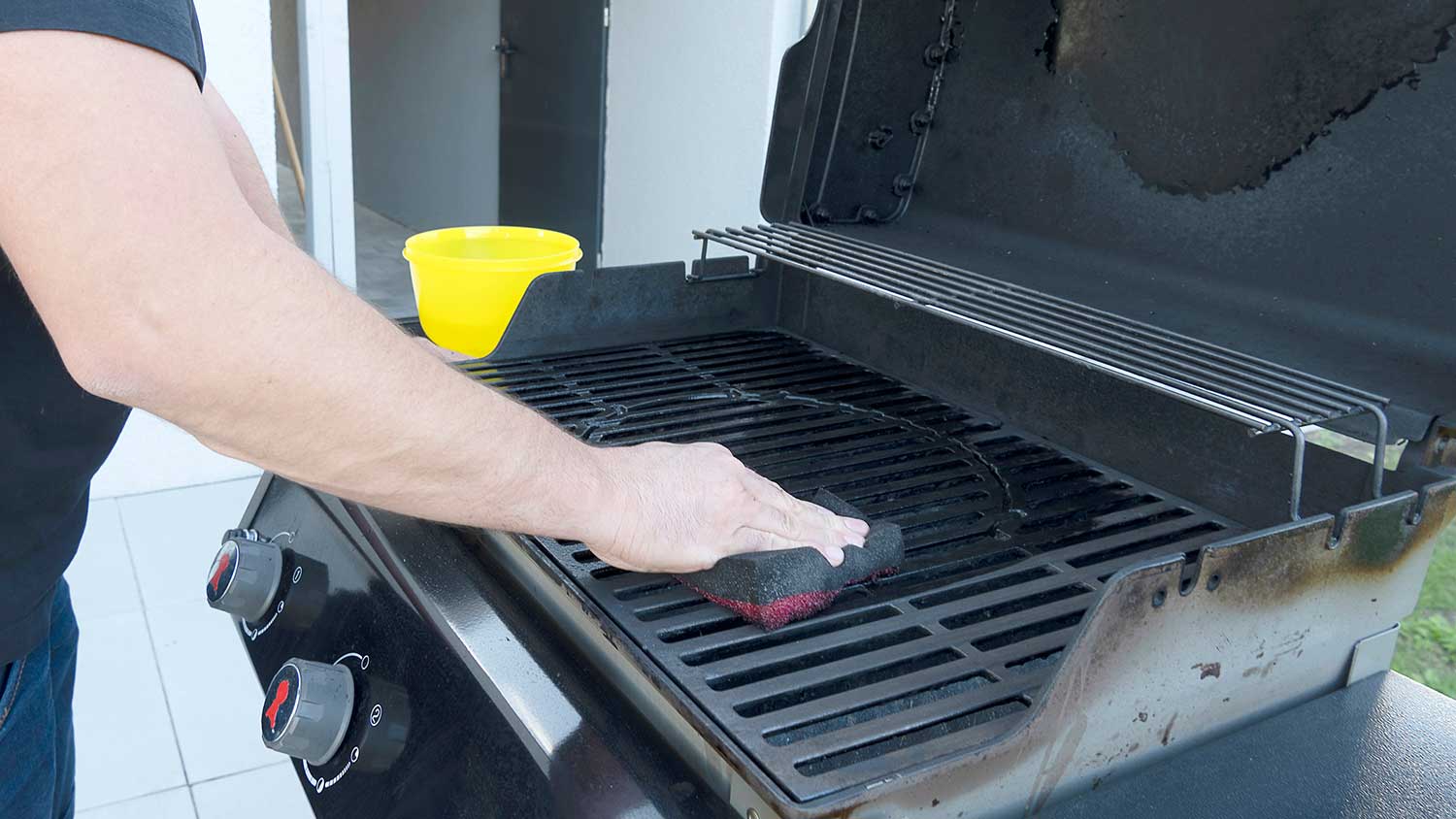 Man scrubbing grill with soap and sponge