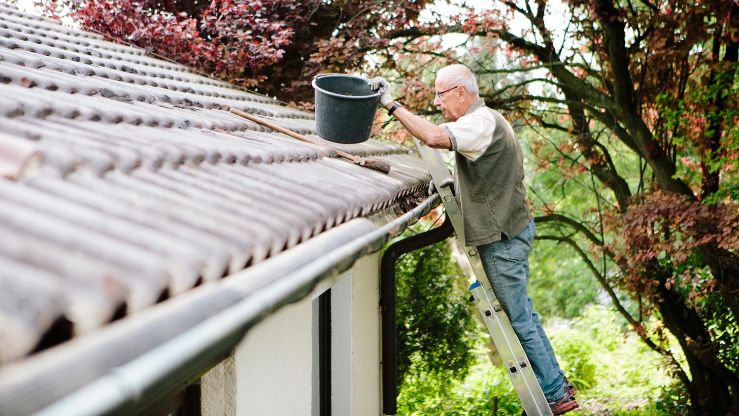 A senior man on a ladder cleaning the gutters