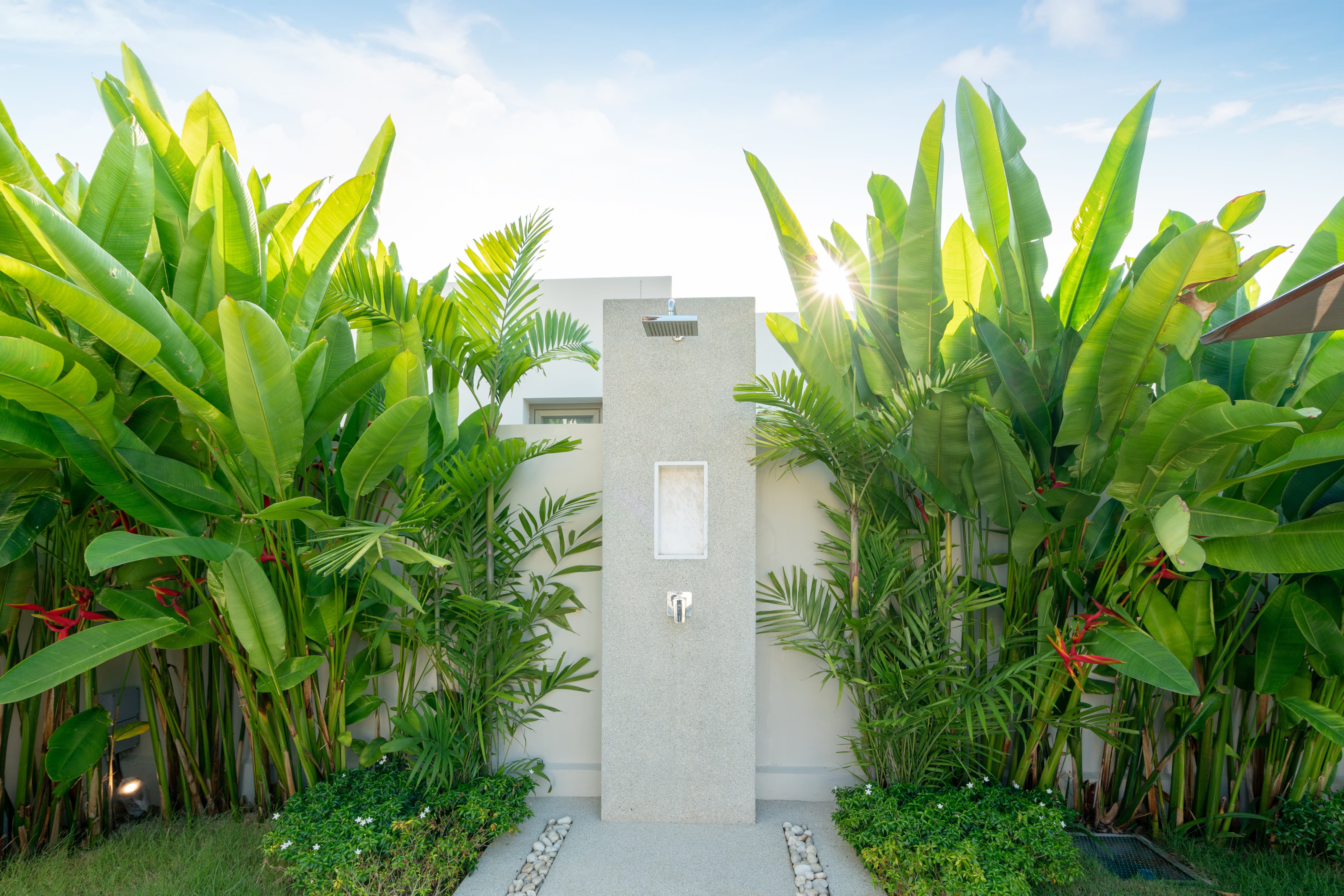 A luxury outdoor shower with a stone and concrete platform surrounded by tall tropical plants