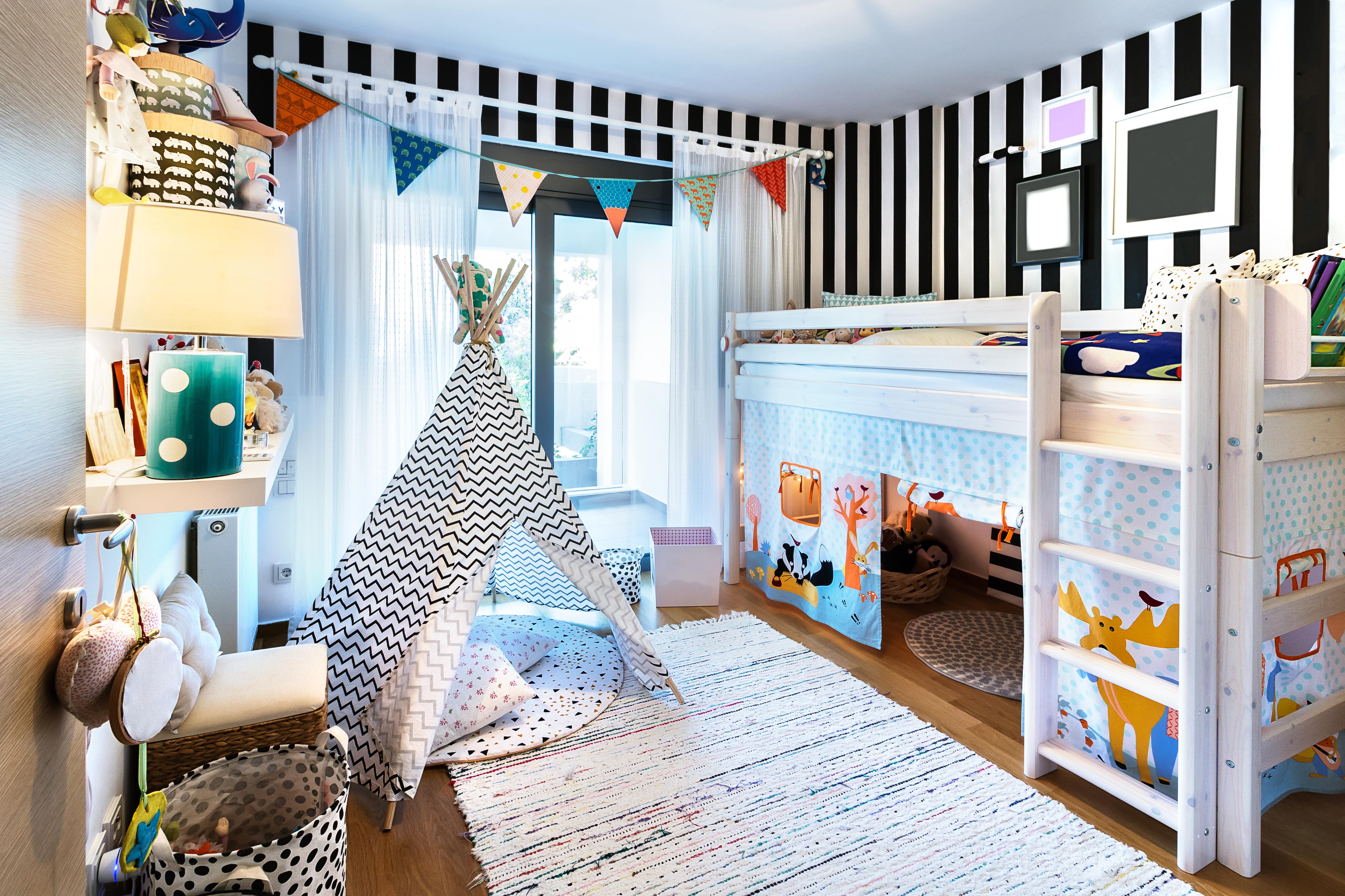 A kid’s bedroom with a bunk bed, tent, and black and white striped walls