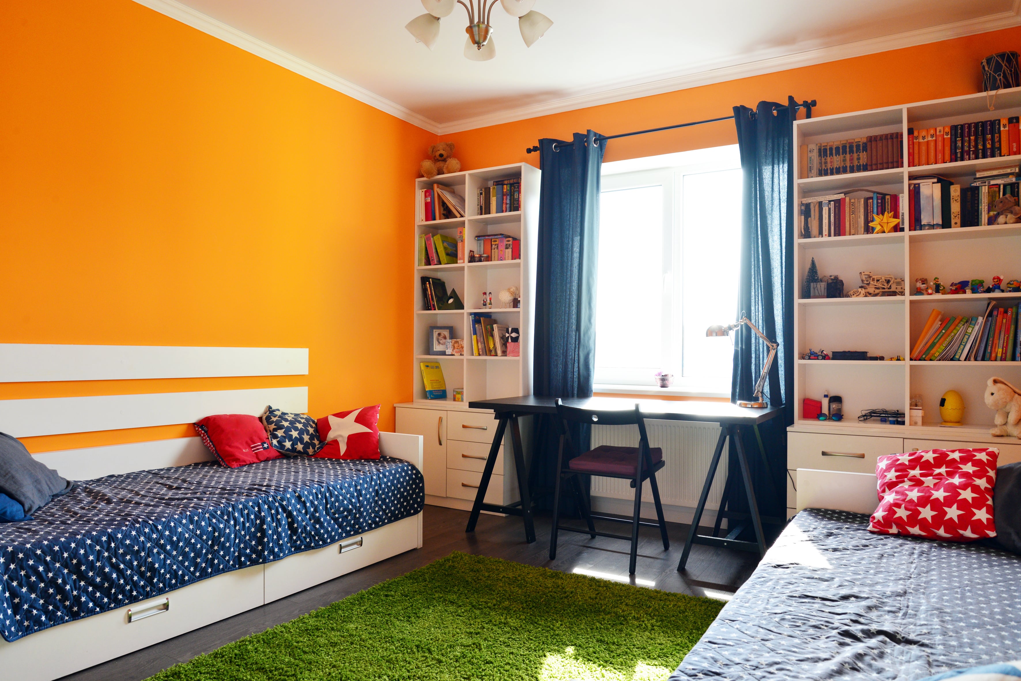 A kids' bedroom with orange walls and blue curtains