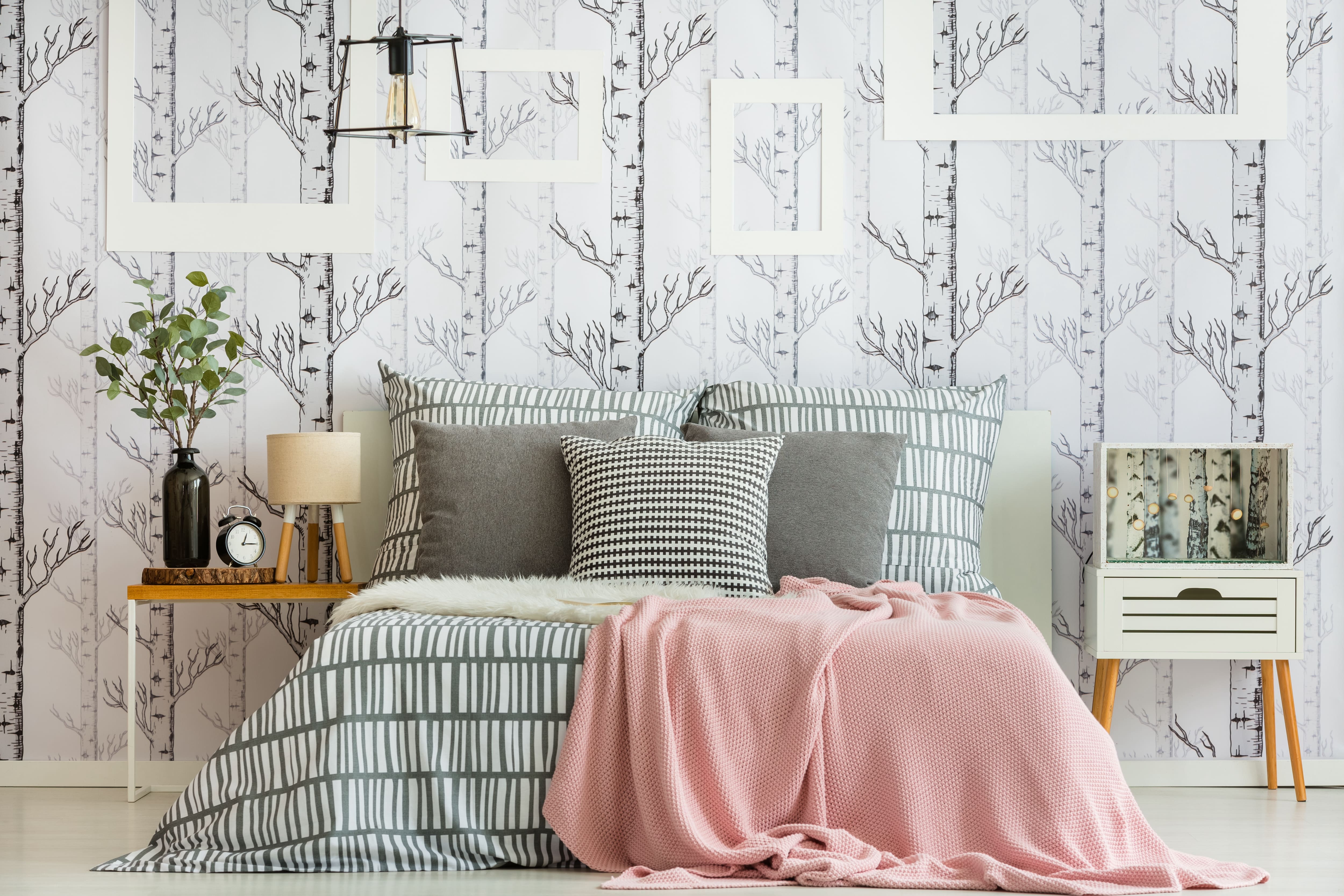 Bedroom with forest wallpaper, graphic black-and-white bedding, and a pink bed blanket