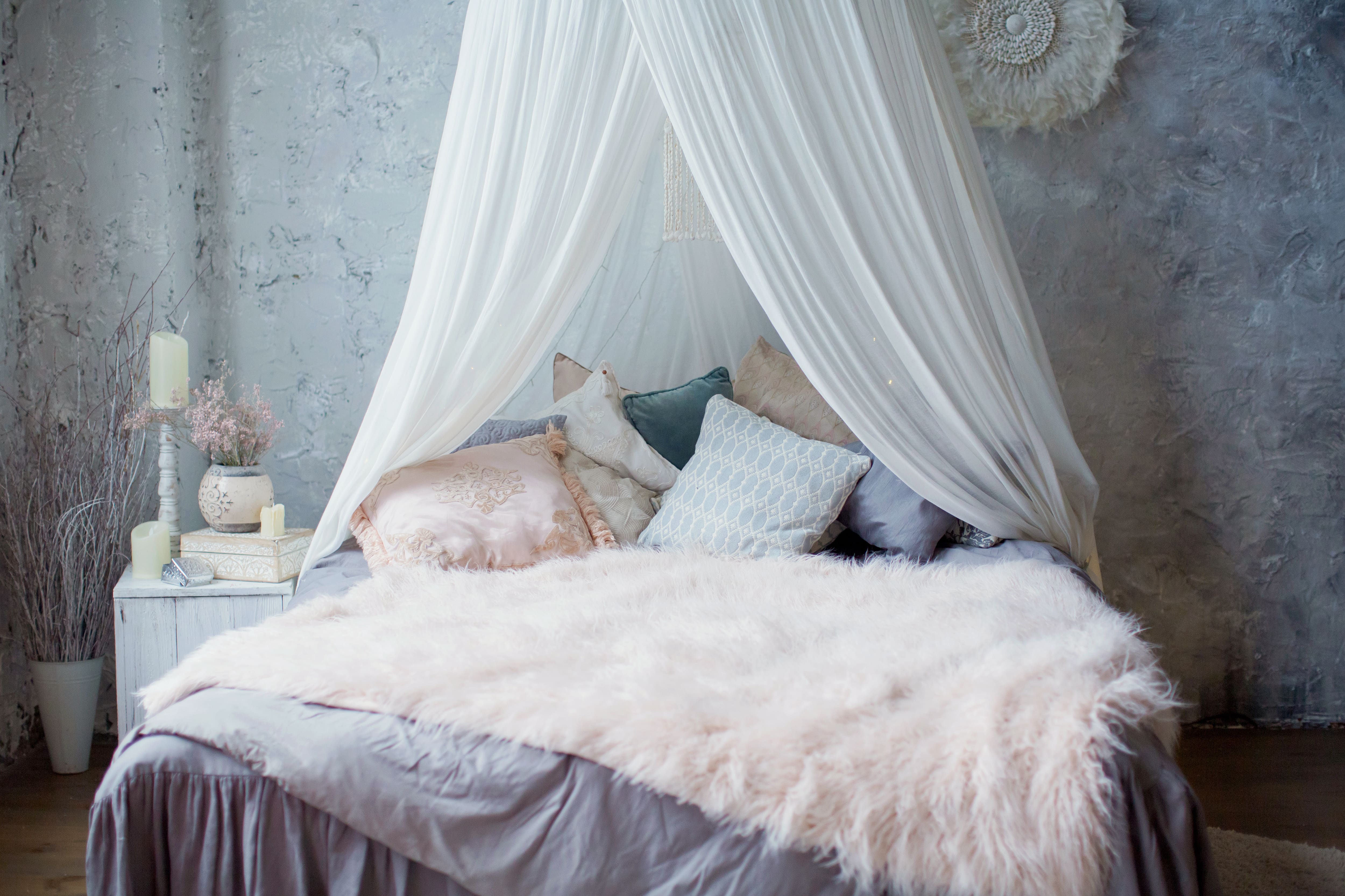 Bed with white canopy, dark gray bedding, pink and gray throw pillows, and pink faux fur throw