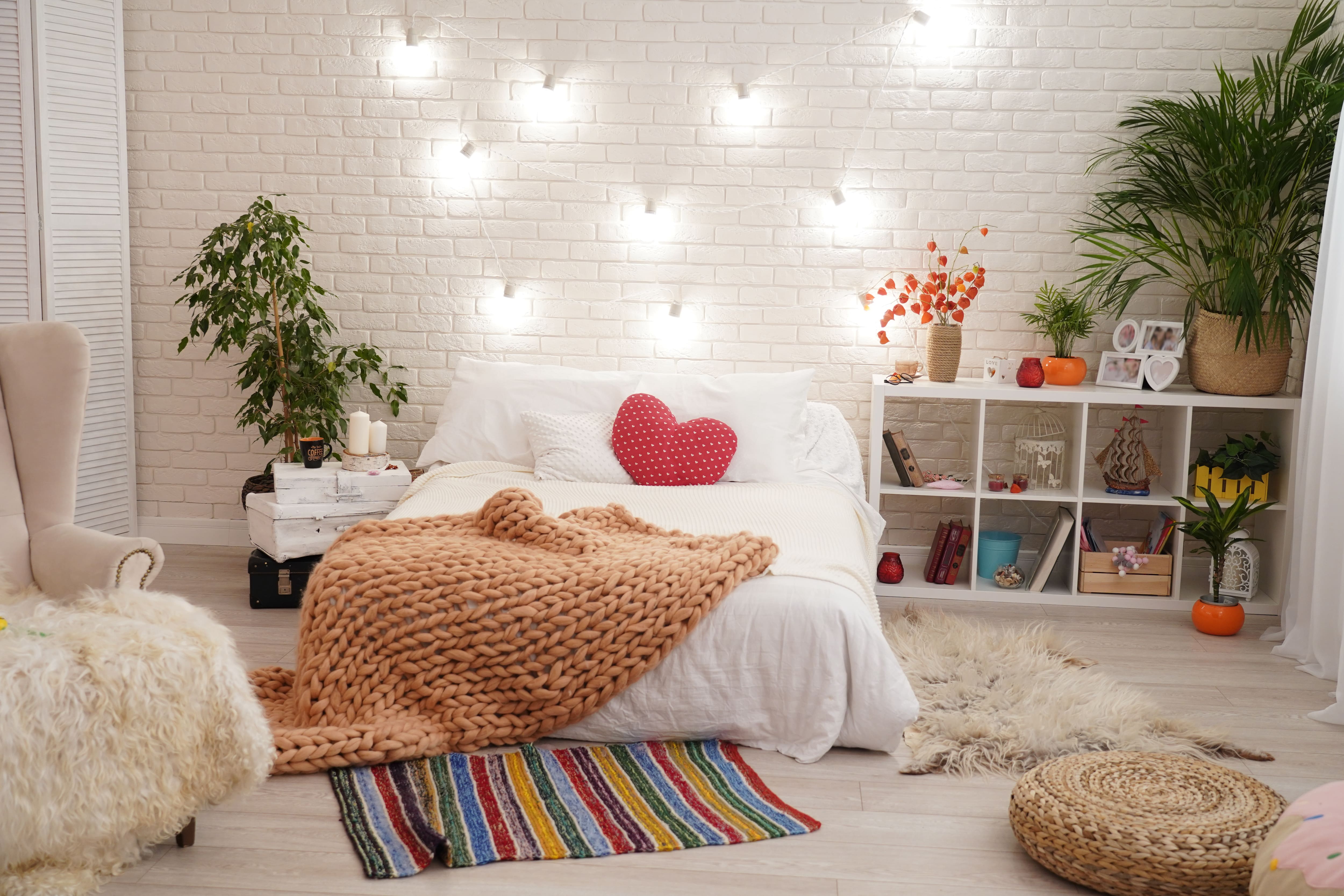 Bedroom with white brick wall, white bedding, knit and fur throws, red heart pillow, and plants