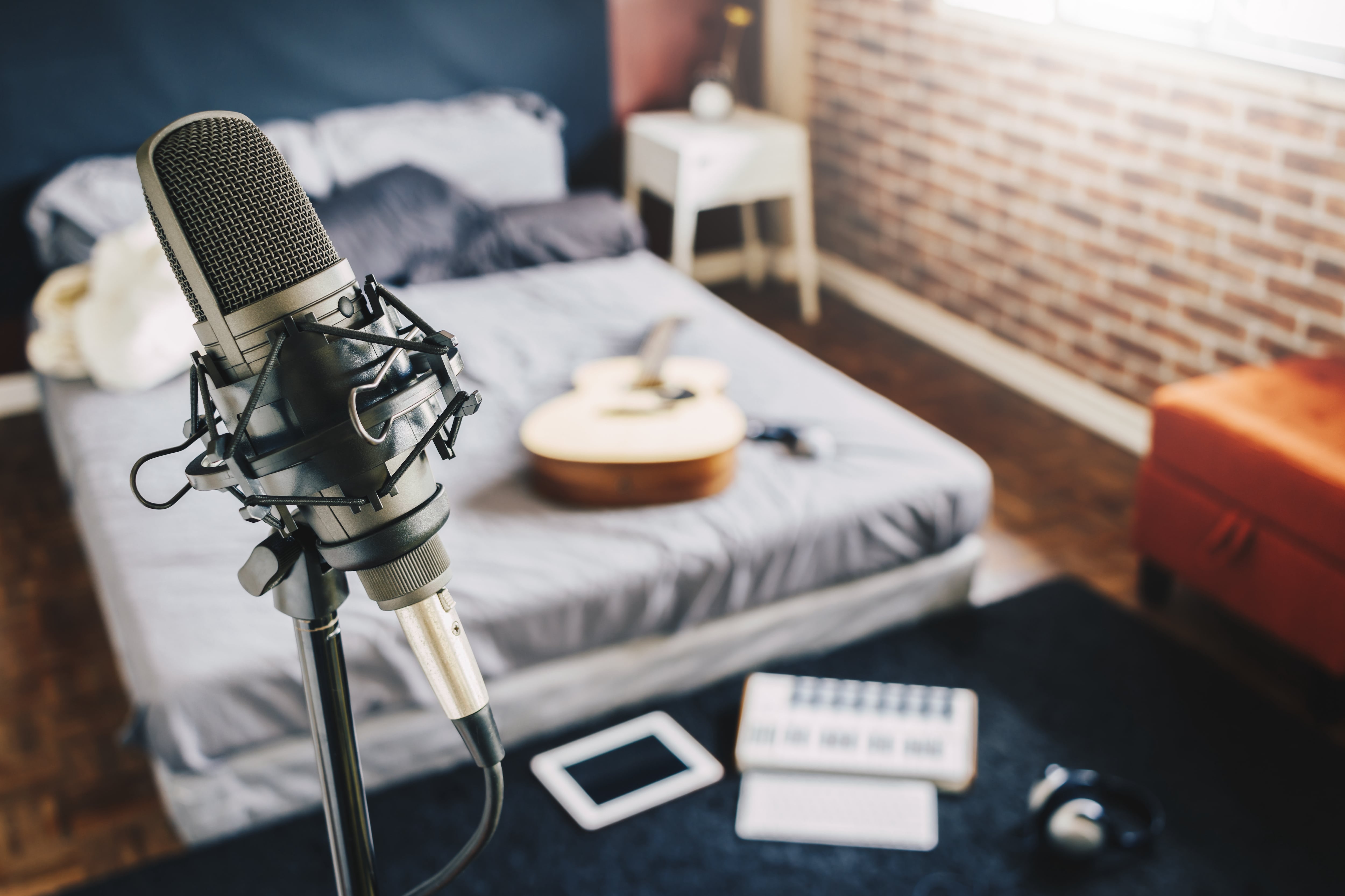 Bedroom recording studio with microphone stand and guitar on the bed in the background