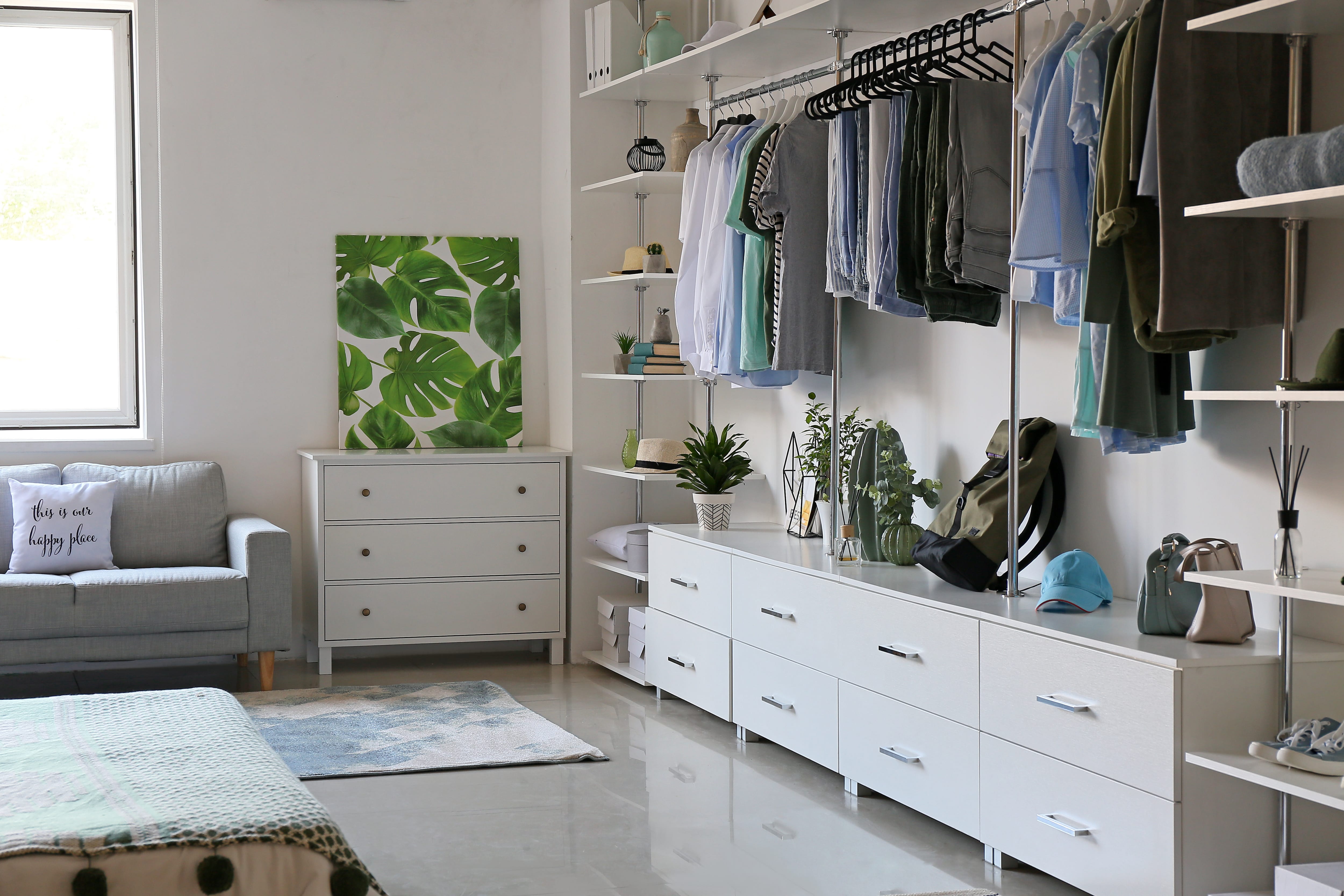 White modern bedroom with storage wall of shelves, a short dresser, and clothing racks