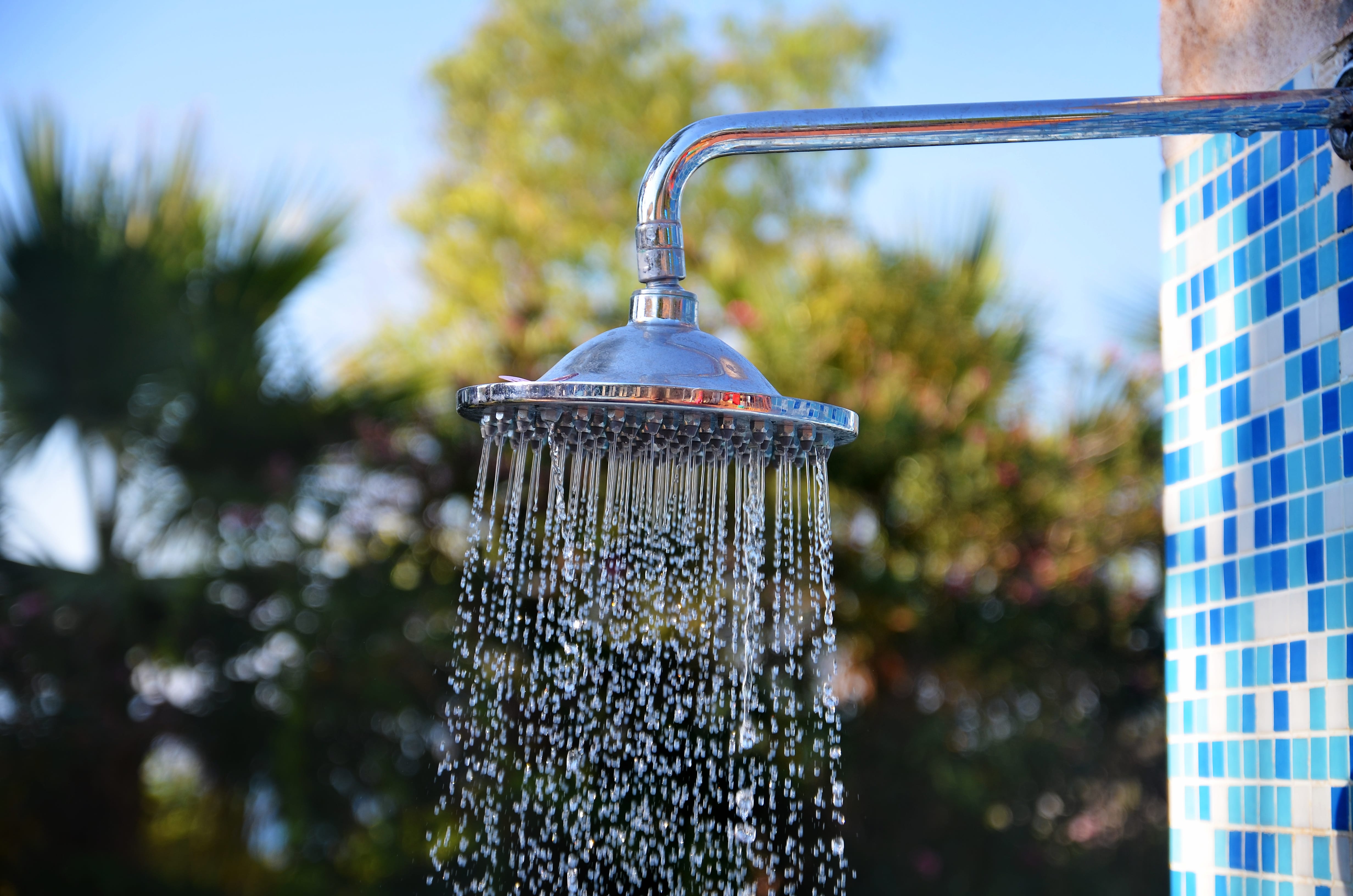 An extended metal rainfall showerhead outdoors with a tile backdrop