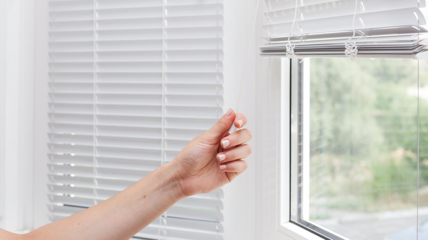 A woman adjusting the white blinds