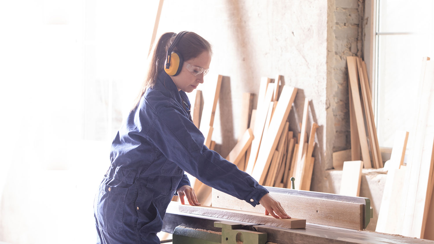 Woman wearing safety gear cutting wooden boards