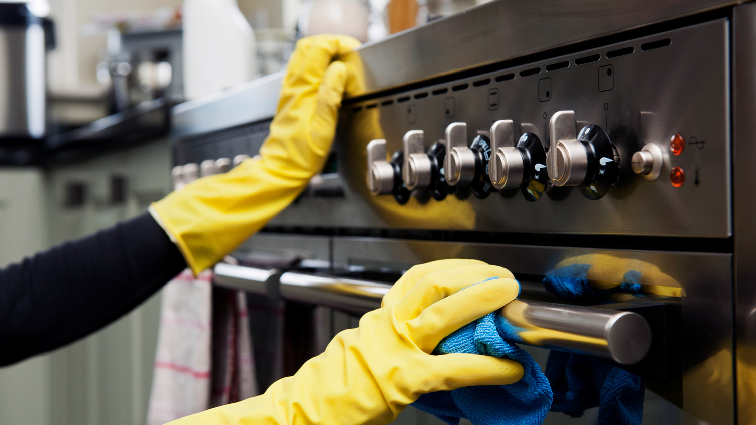A woman in protective gloves cleaning a stainless steel stove