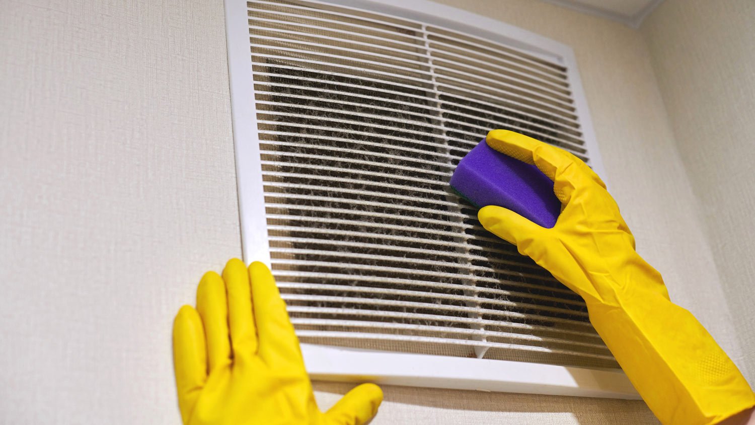 A woman’s hands in gloves while cleaning an air duct with a sponge