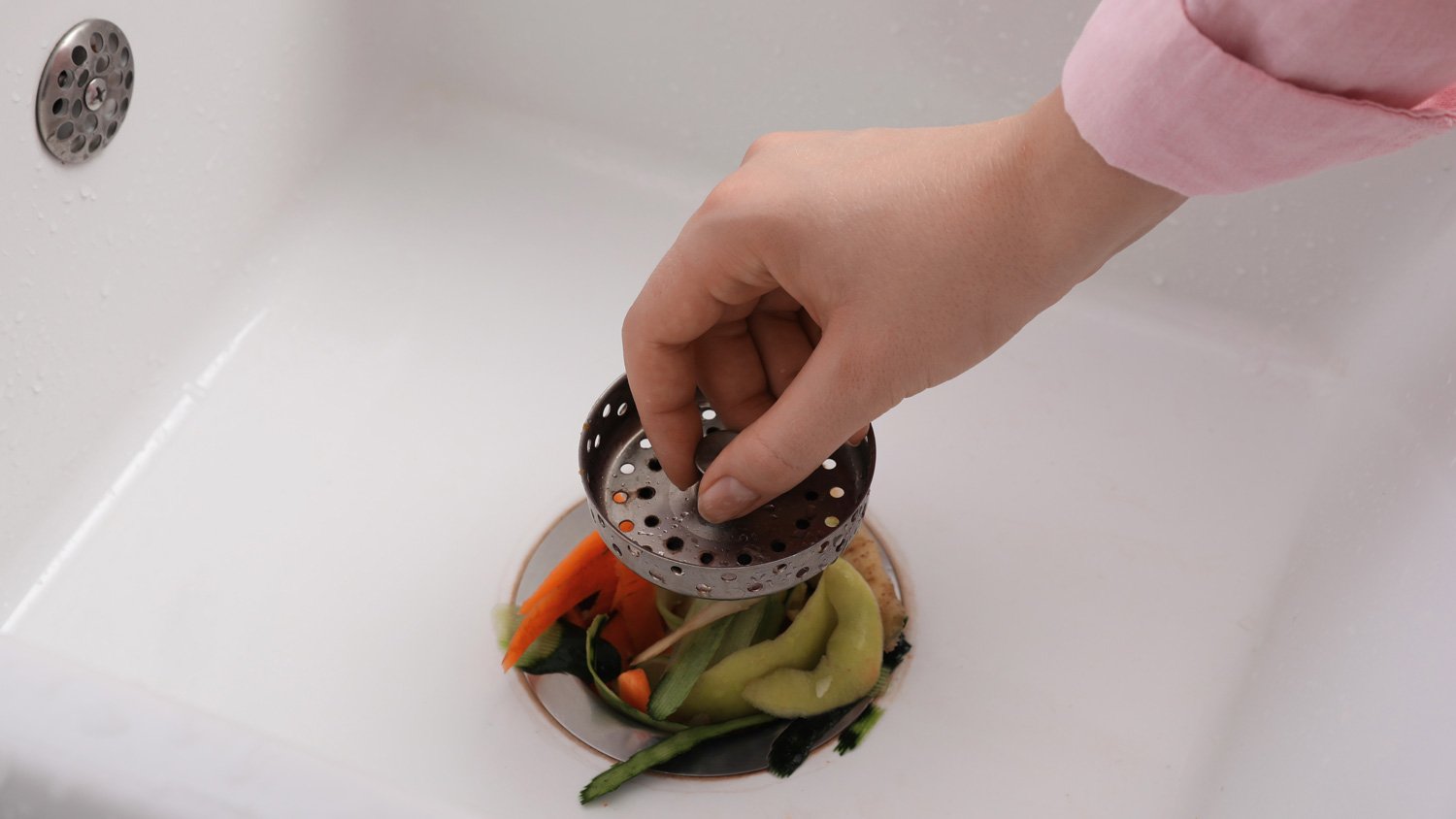 A woman pressing a few vegetable sinks down a garbage disposal