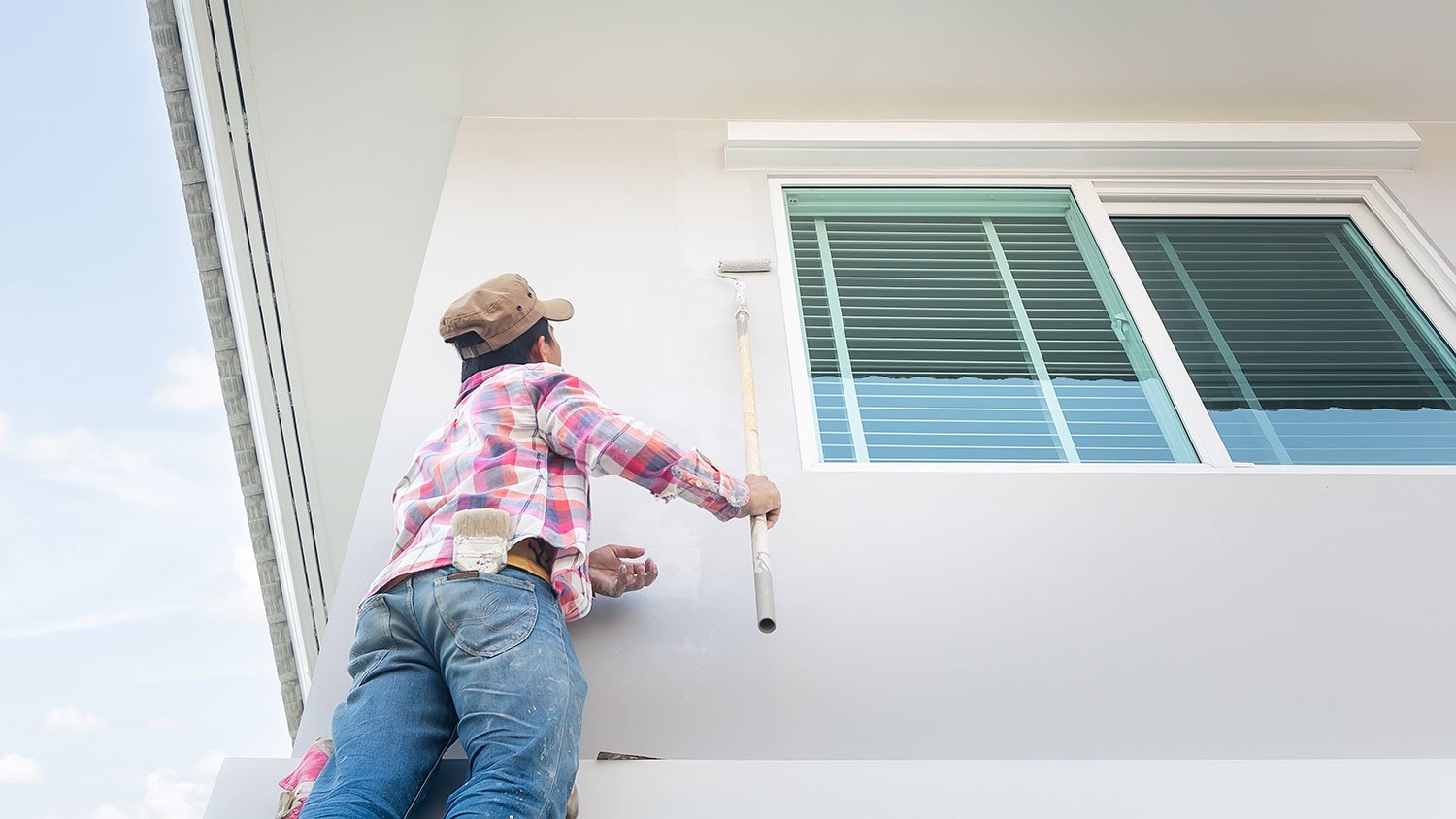 Worker painting tall wall with a brush extension