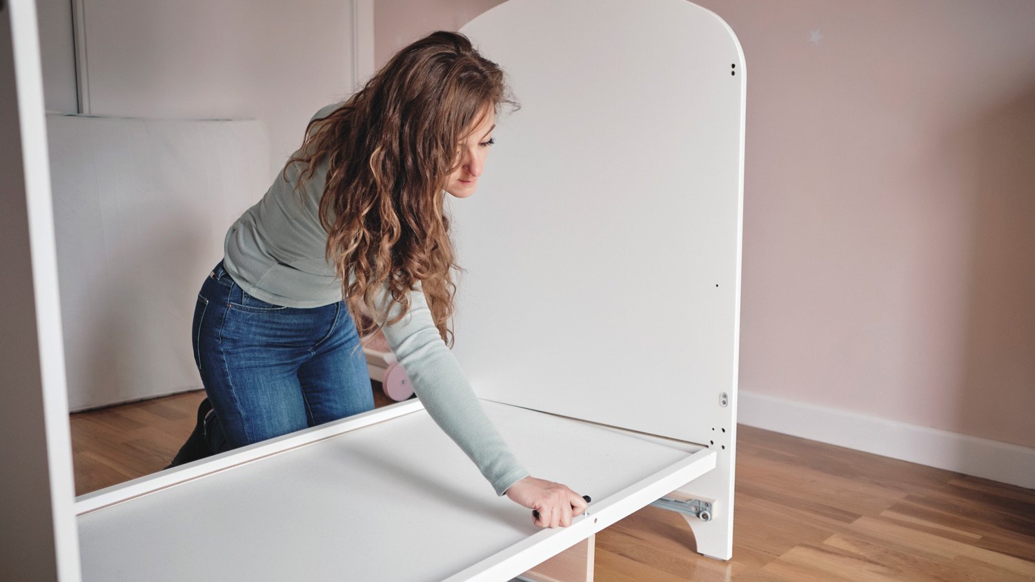 A young woman dismantling a baby crib