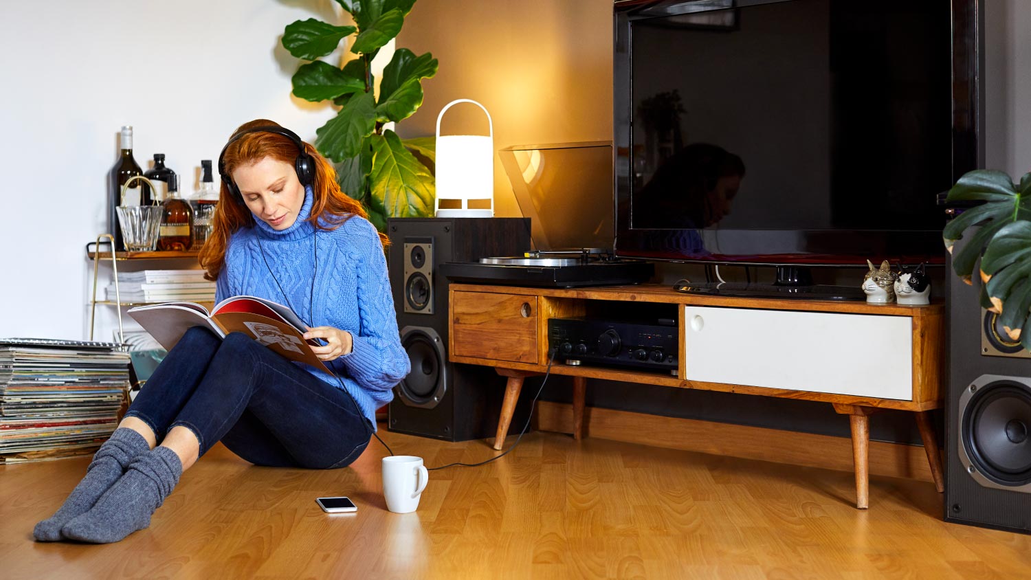 woman sitting on floor with headphones reading book by TV